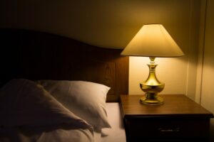Bedside lamp switched on in a dark room with bed turned down