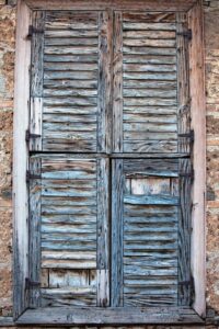 Old and wornout closed wooden plantation shutters on stone home