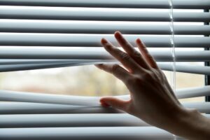 Woman's hand making space between ventetian blinds to peek outside.